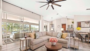 A spacious living room with a large sectional sofa, a round coffee table, and a dining area with a table and chairs. - Infinity Escape - 3BR with Boat Dock and Southern Exposure (Cape Coral)