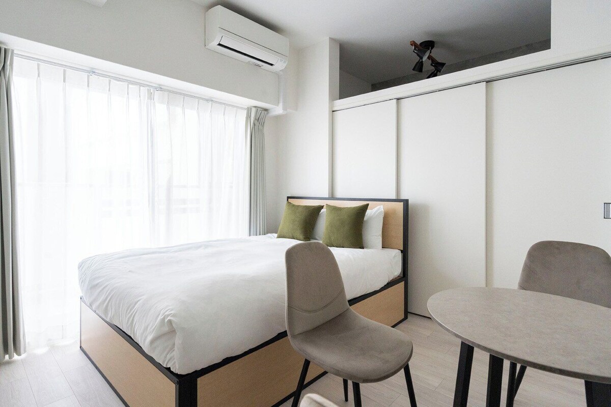 A modern hotel room with a bed, a chair, a table, and an air conditioning unit.