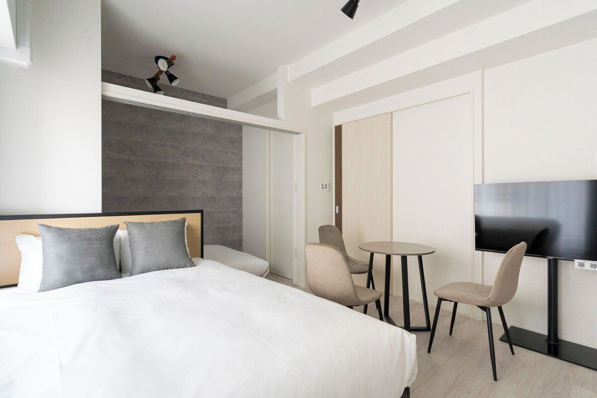 A modern hotel room with a bed, a TV, a small round table, and two chairs.