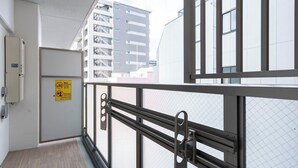 Un balcon avec une rambarde en métal, une porte avec une pancarte et, au loin, la vue d’un immeuble.