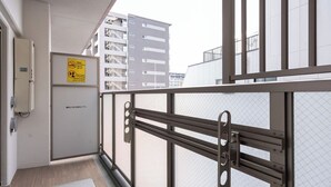 Un balcon avec une rambarde en métal, une porte ornée d’un panneau « interdiction de fumer » et, au loin, la vue sur un immeuble.