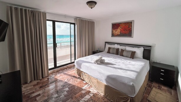 Habitación de hotel con cama, un cuadro, vista al océano y piso de baldosas.