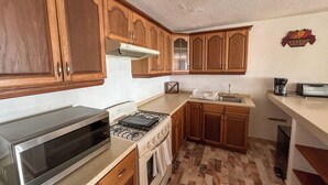 Una cocina con gabinetes de madera, estufa, microondas y pileta.