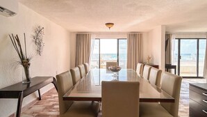Un comedor amplio con una mesa larga y sillas, ventanas grandes con cortinas, y vista al mar.