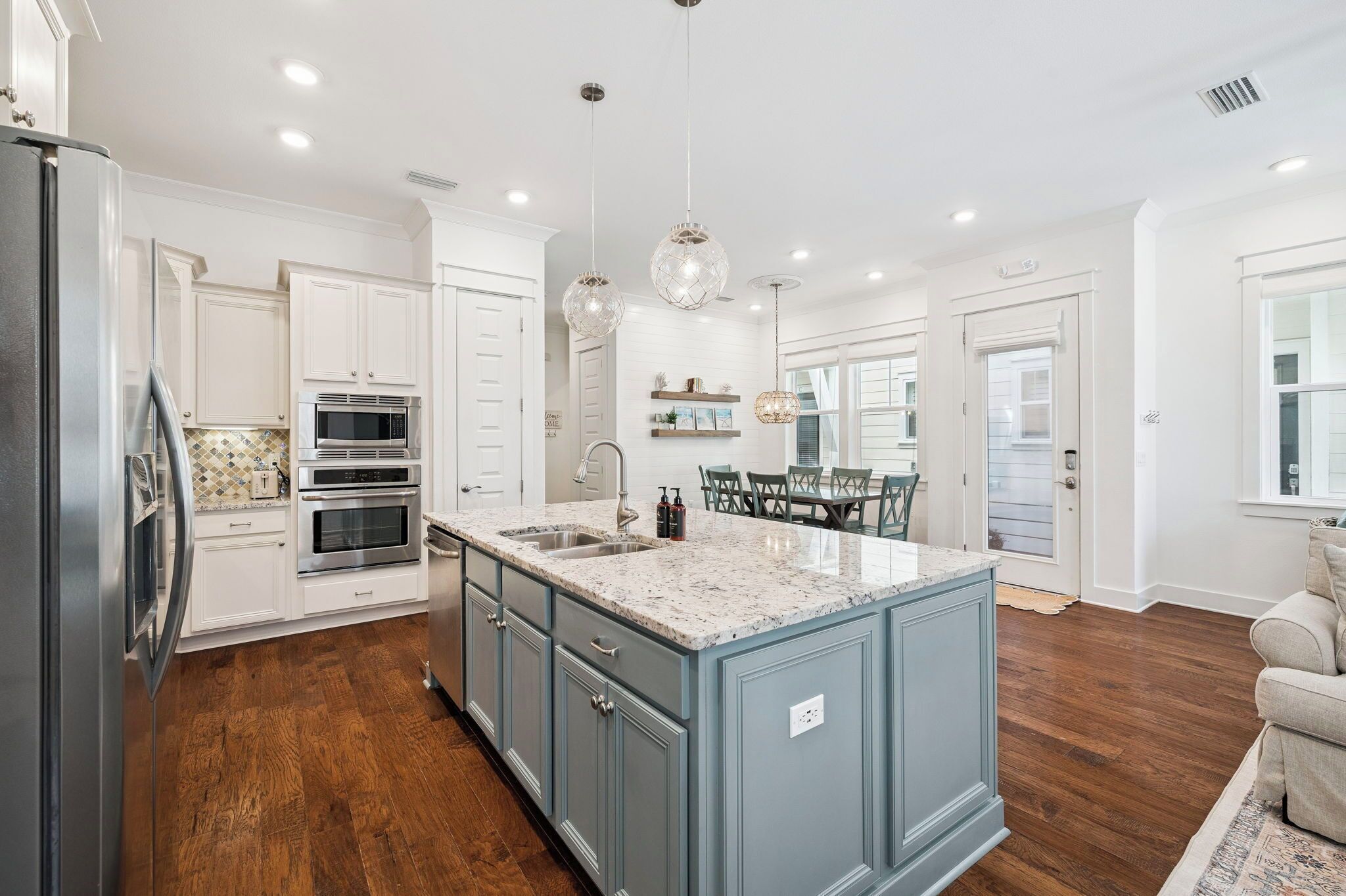 A kitchen with white cabinets, a granite countertop, a central island, and a dining area with a table and chairs.