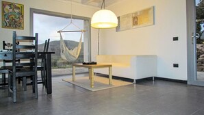 Un interior moderno con comedor, una silla colgante, un sofá y un ventanal grande.