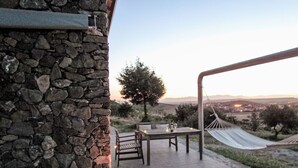 Un muro de piedra, una mesa de madera con sillas, una hamaca y vistas al campo.
