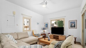 Ein Wohnzimmer mit Sofa, Sessel, Fernseher und einem Fenster mit Blick.