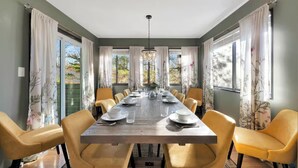 A dining room with a long table, yellow chairs, and floral curtains. - 5BR Resort-Style - Game Room, Hot Tub, Fire Pit (East Stroudsburg)