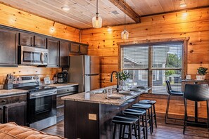 A modern kitchen with stainless steel appliances, wooden cabinetry, and a central island with bar stools. - Just Remodeled Cabin w/ 4-Game Arcade, Hot Tub & Peloton | 4 Mi to Dollywood! (Pigeon Forge)