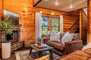 A cozy cabin interior with a fireplace, wooden walls, a sofa, and a dining table. - Just Remodeled Cabin w/ 4-Game Arcade, Hot Tub & Peloton | 4 Mi to Dollywood! (Pigeon Forge)