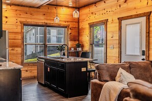 A cozy cabin interior with a wooden exterior, a kitchen with a central island, and a seating area with a couch. - Just Remodeled Cabin w/ 4-Game Arcade, Hot Tub & Peloton | 4 Mi to Dollywood! (Pigeon Forge)