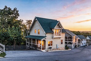 Une maison en bois à deux étages, dotée d’un toit à pignon, d’un porche couvert et d’une allée bordée de clôtures.