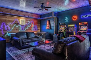 Quarto com teto de madeira, letreiros de neon, mesa de futebol de mesa e jogos de fliperama.