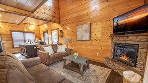 Een gezellig interieur van een chalet met een open haard, een televisie, een bank en een keukenhoek.