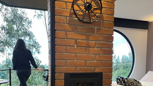 Una habitación moderna con chimenea de ladrillo, un ventanal grande, una cama y una mesa con tazas.
