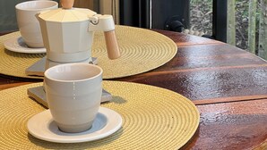 Una mesa de madera con una cafetera, tazas y una cuchara de madera.