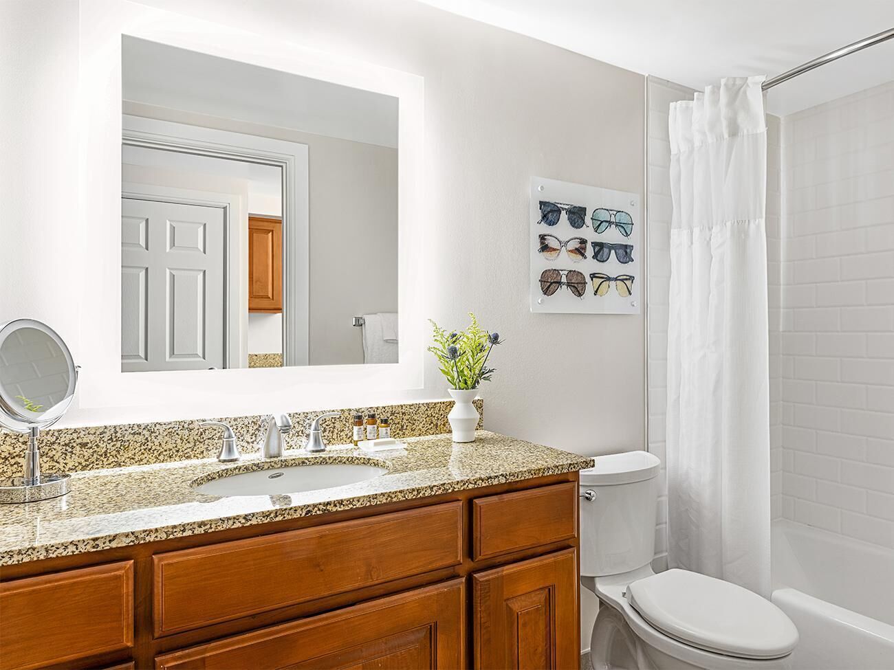 Une salle de bain avec un comptoir en granit, un lavabo blanc, un miroir, des toilettes et un rideau de douche.