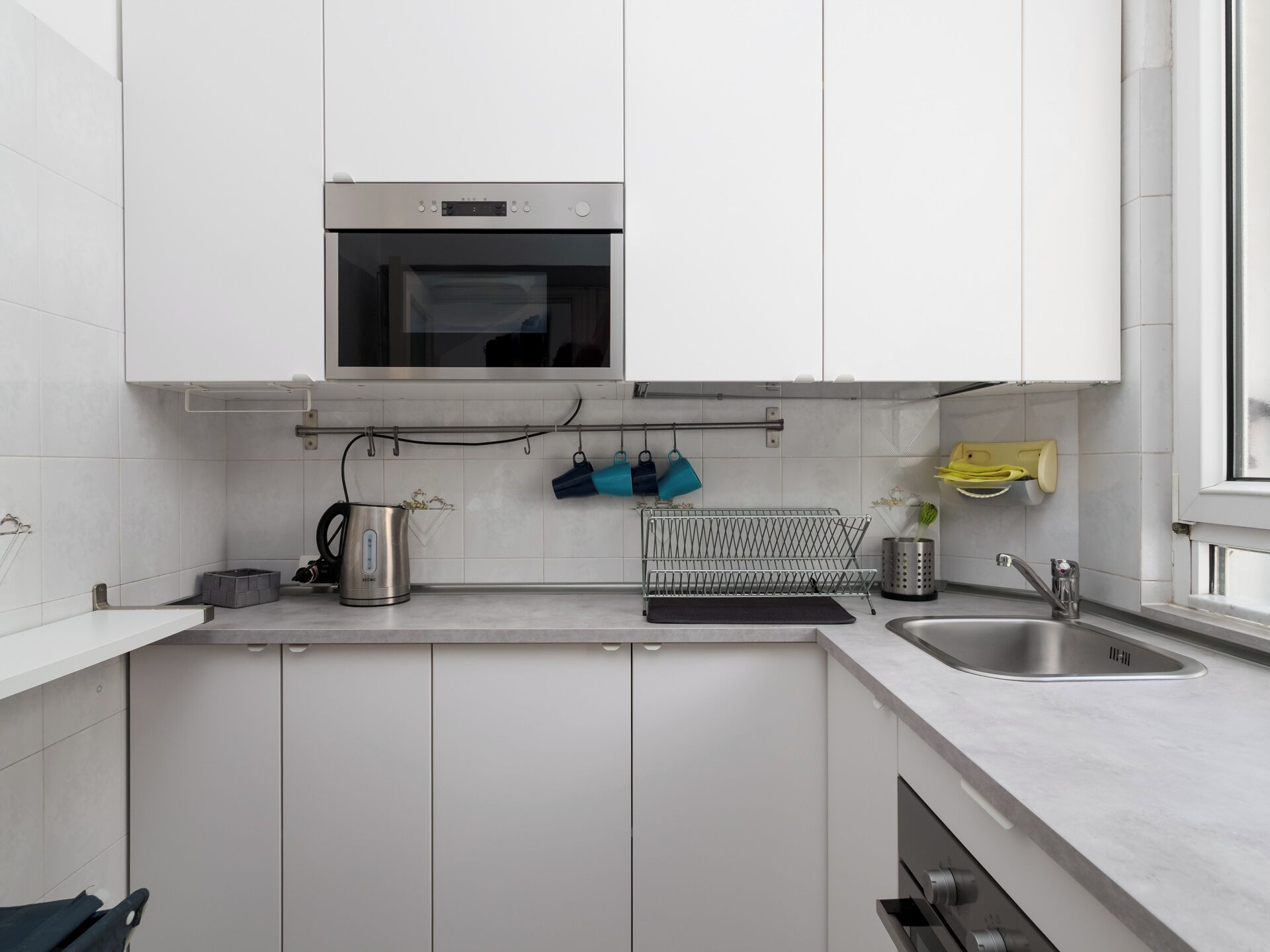 A modern kitchen with white cabinets, a stainless steel oven, a kettle, and a drying rack.