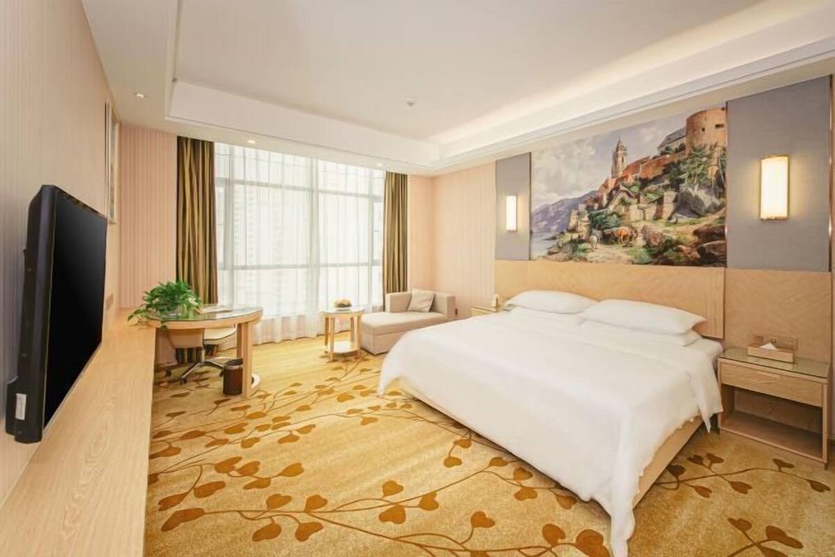 Une chambre d’hôtel avec un grand lit, un bureau, une chaise, une télévision et un tableau au mur.