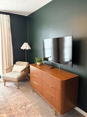 Une pièce comprenant un meuble en bois, une chaise, une plante en pot, une lampe et un téléviseur à écran plat fixé au mur.