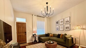 Ein Wohnzimmer mit Ecksofa, Couchtisch, einer Kandelaberleuchte, einer Stehlampe und gerahmten Bildern an der Wand.
