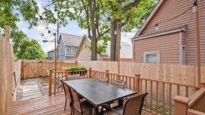 A wooden deck with a table and chairs, surrounded by a wooden fence and trees. - Steps to Mass Ave • Sleeps 9 • Free Parking (Indianapolis)