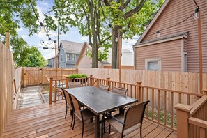 Une terrasse en bois avec une table et des chaises, entourée d’une clôture en bois et d’arbres.