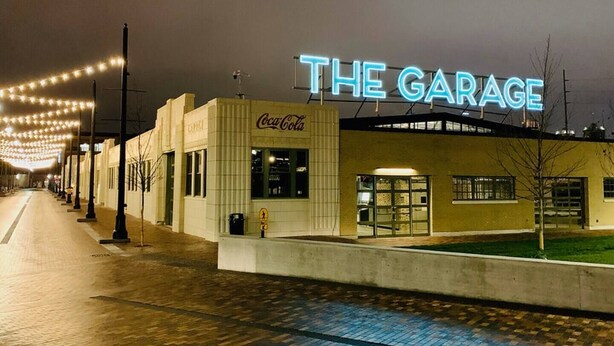 A building with a neon sign reading 'THE GARAGE' and a Coca-Cola sign on the side. - Steps to Mass Ave • Sleeps 9 • Free Parking (Indianapolis)
