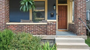 A brick house with a front porch, a door, and a hanging plant. - Steps to Mass Ave • Sleeps 9 • Free Parking (Indianapolis)