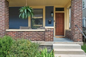 Une maison en briques avec un porche à l’avant, une porte et une plante suspendue.