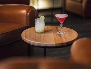 A round wooden table with two drinks, one in a glass and one in a jar, in a room with leather furniture. - Eklo Hotels Montpellier Centre Gare (Montpellier)
