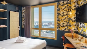 A hotel room with a bed, a desk, a chair, a TV, and a window with a city view. - Eklo Hotels Montpellier Centre Gare (Montpellier)