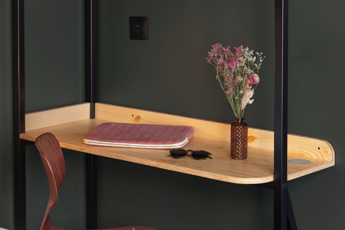 A wooden desk with a notebook, sunglasses, and a vase of flowers.