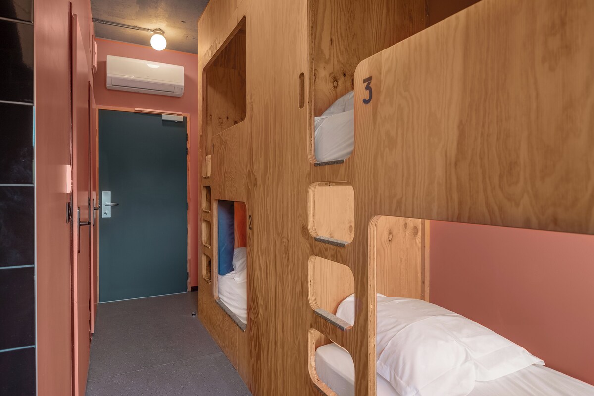 A room with bunk beds, numbered 2 and 3, wooden walls, and a door leading to another room.