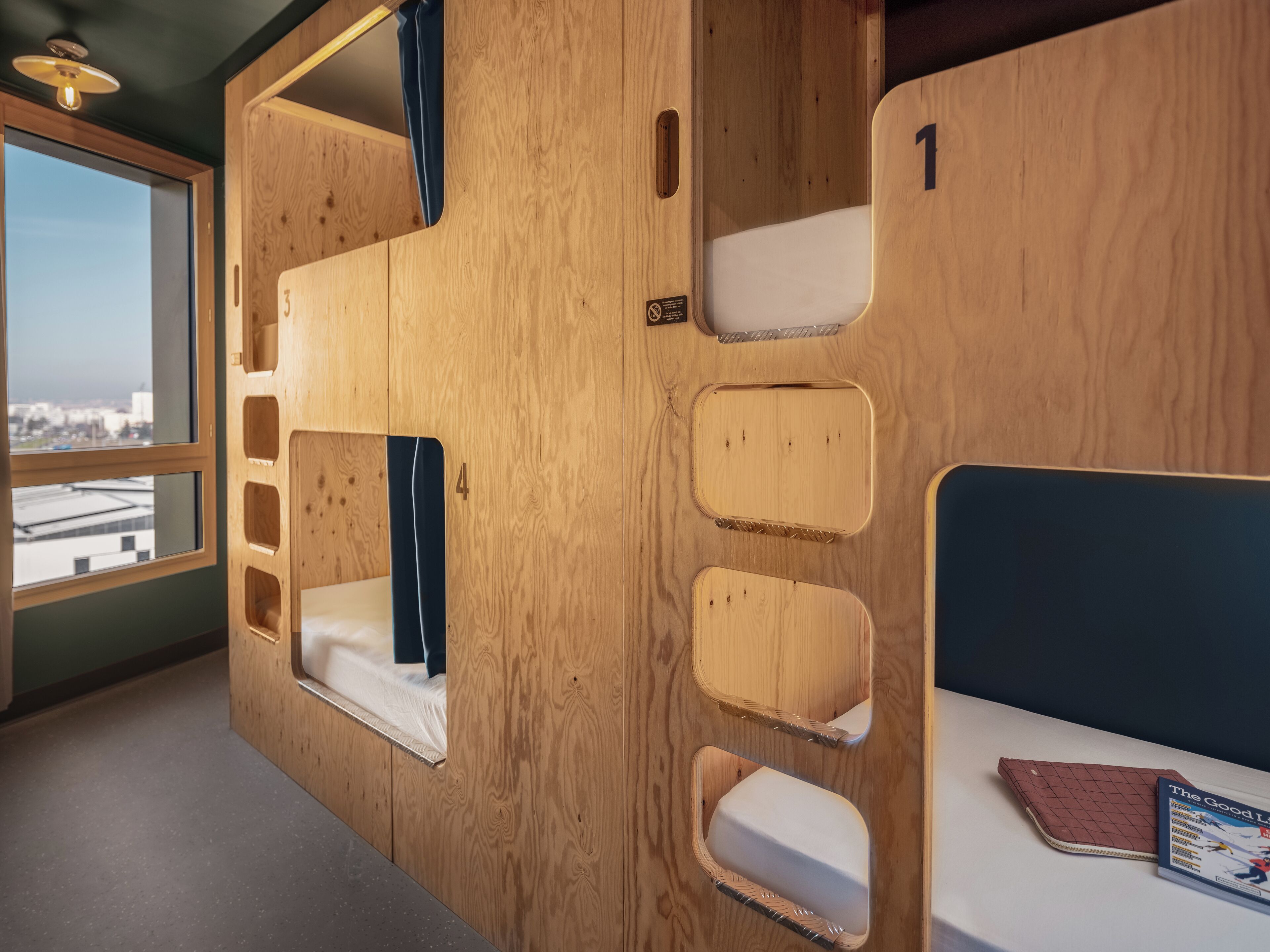 A wooden bunk bed with a window, a desk with a chair, and a book on the desk.