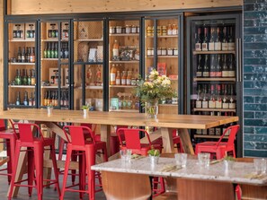 A bar area with wooden tables and red chairs, shelves with bottles and jars, and a vase with flowers on the table. - Eklo Hotels Montpellier Centre Gare (Montpellier)