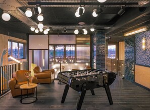A modern indoor space with a foosball table, leather sofas, a bar area, and large windows offering a city view. - Eklo Hotels Montpellier Centre Gare (Montpellier)
