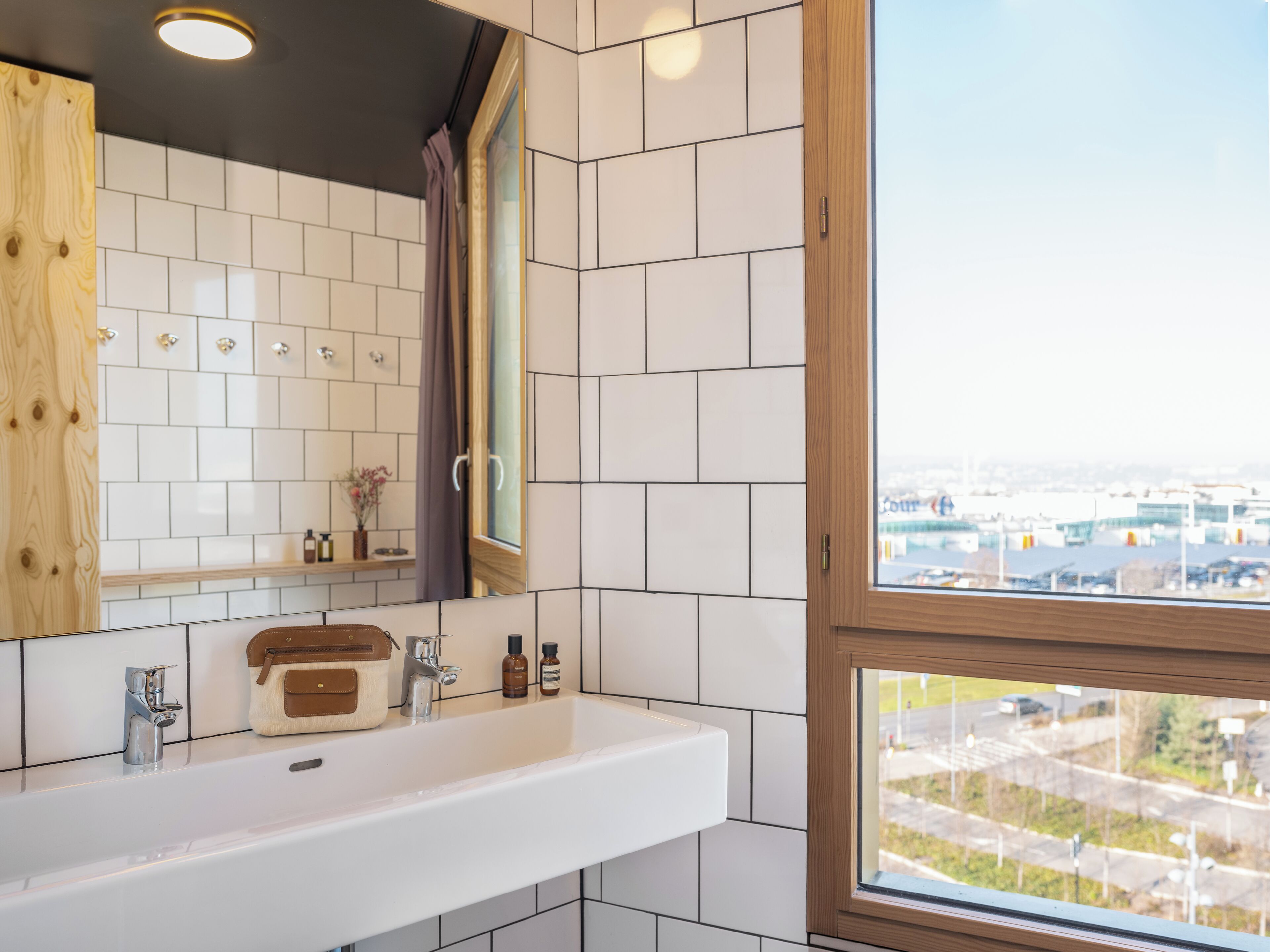 A bathroom with a white sink, wooden cabinet, and a window with a city view.
