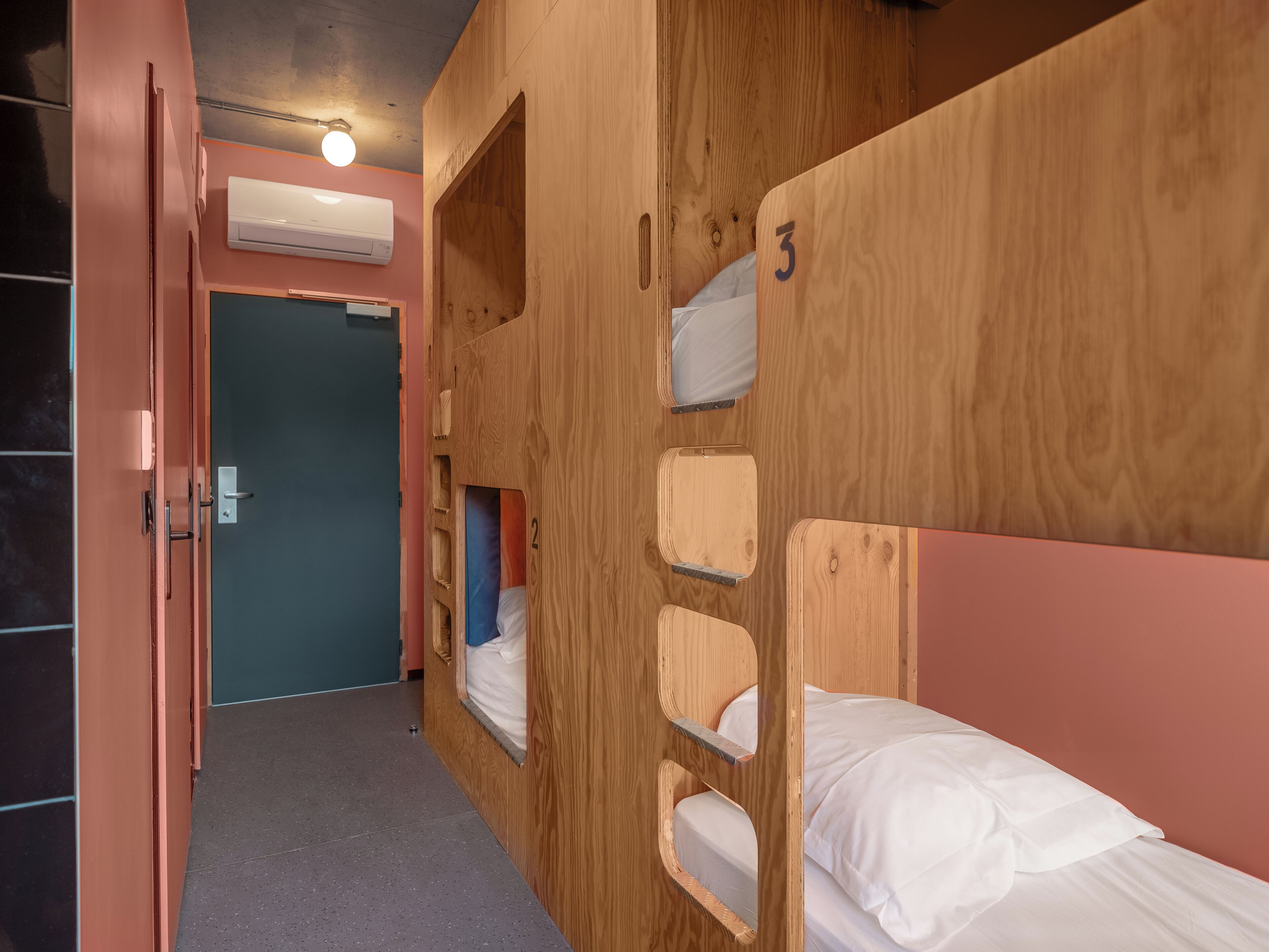 A room with bunk beds, numbered 2 and 3, wooden walls, and a door leading to another room.