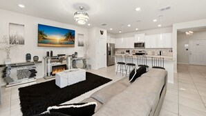 Een moderne woonkamer met een open haard, een groot schilderij en een keuken met barkrukken.