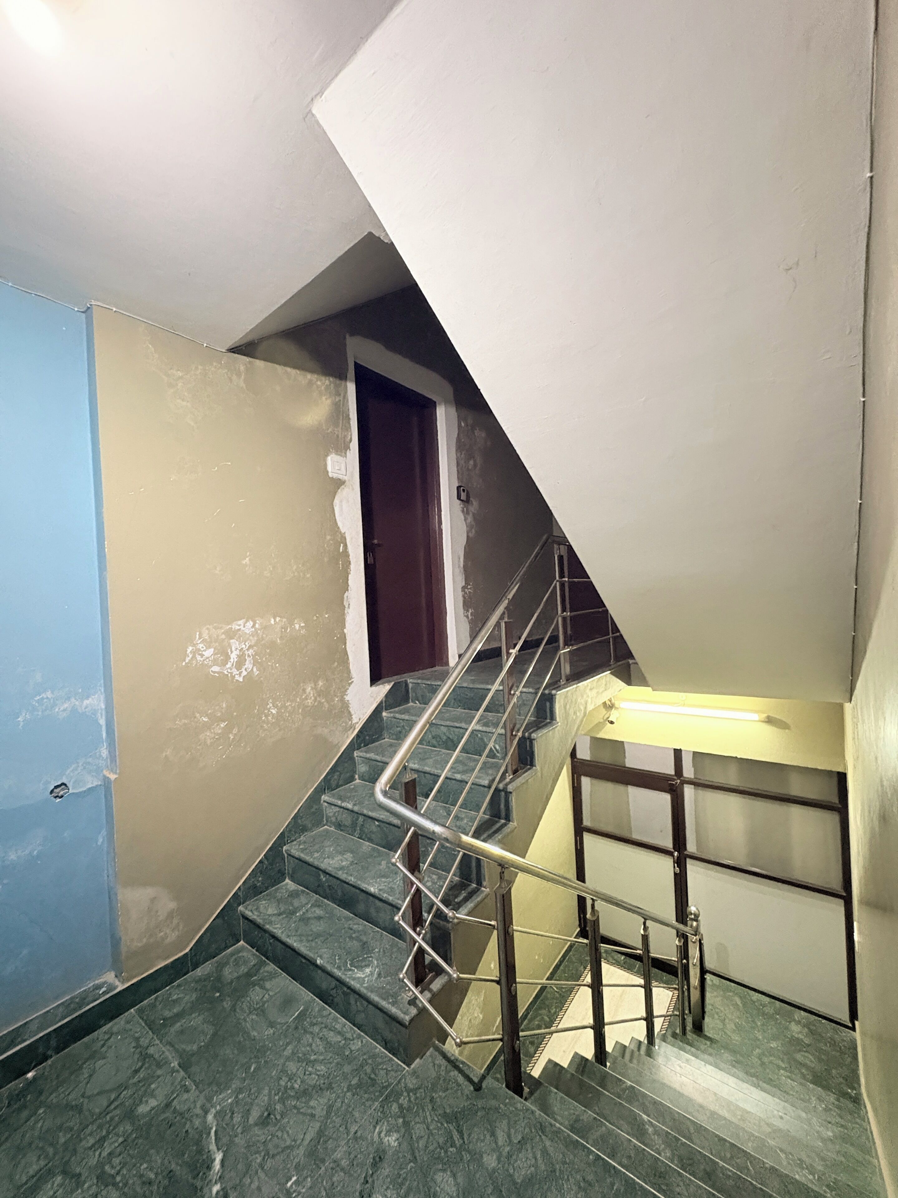 Un escalier avec des rampes en métal, une porte en haut et un mur bleu d’un côté.