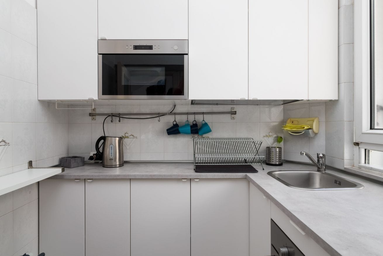 Una cocina moderna con armarios blancos, horno de acero inoxidable, hervidor y pileta.