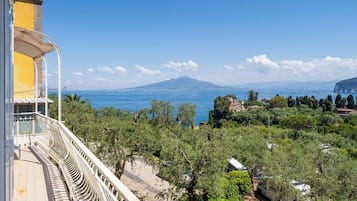 Un balcon avec vue sur la mer, une montagne à l’horizon et un bâtiment à la façade jaune.