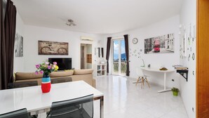 A modern living room with a sofa, TV, dining table, and chairs. - Casa Rosa is one of those places you choose for one specific detail… and then remember for everything else. That detail is the view: a balcony opening onto the Gulf of Naples with Mount Vesuvius in front, a wide, deep panorama that accompanies every mo (Sorrento)