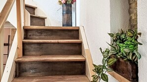 Een houten trap met een witte muur, een hanglamp en een potplant aan de rechterkant.