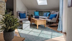 Een gezellig loft slaapkamer met een schuine kap, dakraam, zithoek, bijzettafeltje en een plant in pot.