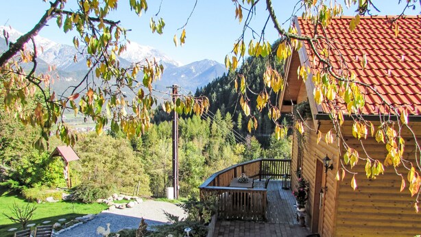 Een houten chalet met een rood pannendak, een terras en uitzicht op bergen.