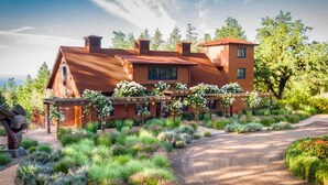 A large, rustic house with a prominent chimney, surrounded by a well-maintained garden and a gravel driveway.