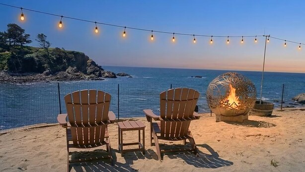 A beach setting with chairs, a fire pit, and string lights.